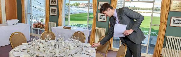 person in suit holding a document while checking if table is set properly